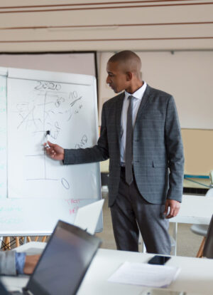 Confident speaker talking and pointing at whiteboard. Group of employees discussing ideas during presentation of new project at briefing. Business meeting concept