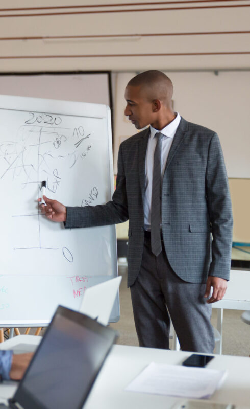 Confident speaker talking and pointing at whiteboard. Group of employees discussing ideas during presentation of new project at briefing. Business meeting concept