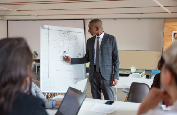 Confident speaker talking and pointing at whiteboard. Group of employees discussing ideas during presentation of new project at briefing. Business meeting concept