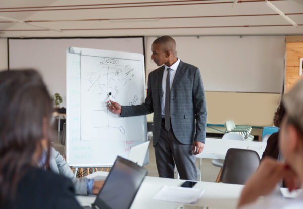 Confident speaker talking and pointing at whiteboard. Group of employees discussing ideas during presentation of new project at briefing. Business meeting concept