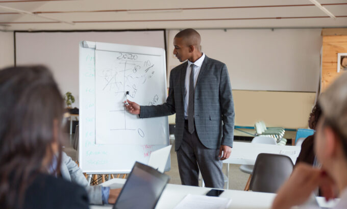 Confident speaker talking and pointing at whiteboard. Group of employees discussing ideas during presentation of new project at briefing. Business meeting concept