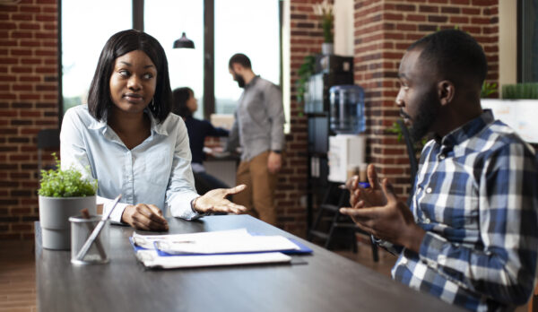 Candidate speaking to hiring manager Young black woman explaining her work experiences and expectations to professional hiring manager. Male recruiter and female candidate engage in a formal discussion in a modern office.